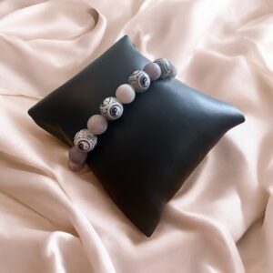 Bracelet lilas avec perles Yin Yang violettes, présenté sur coussin noir en simili cuir posé sur satin rose pâle.